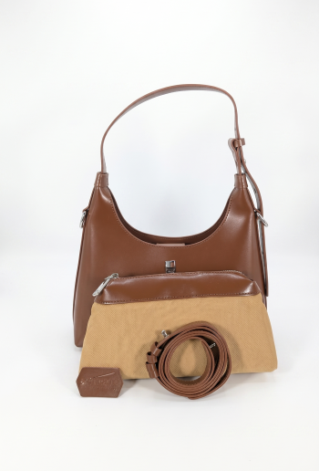 A smooth brown shoulder bag sitting behind a two-toned tan canvas and brown zippered pouch. A neatly coiled brown strap and a small branded tag are arranged in front of the pouch against a plain white background