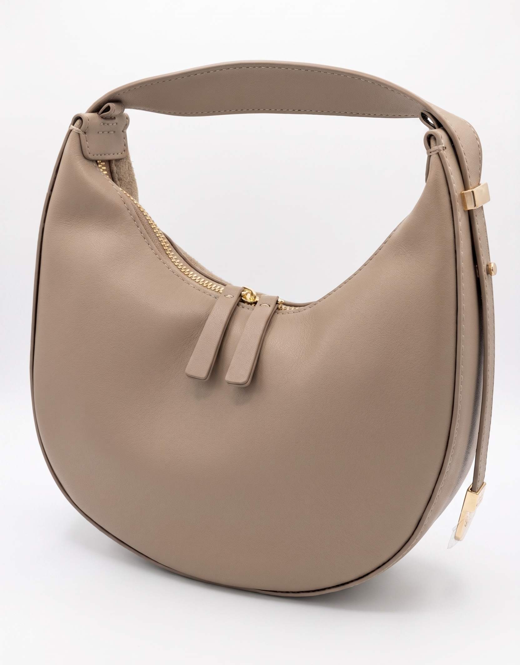 SHUCLUB Luxury Leather Crescent Hobo Bag – Nude Beige A nude beige smooth leather crescent-shaped hobo shoulder bag by SHUCLUB, showcasing a minimalist curved silhouette, dual top zippers with leather pull tabs, and polished gold hardware accents on the side strap, shot against a solid white studio background.