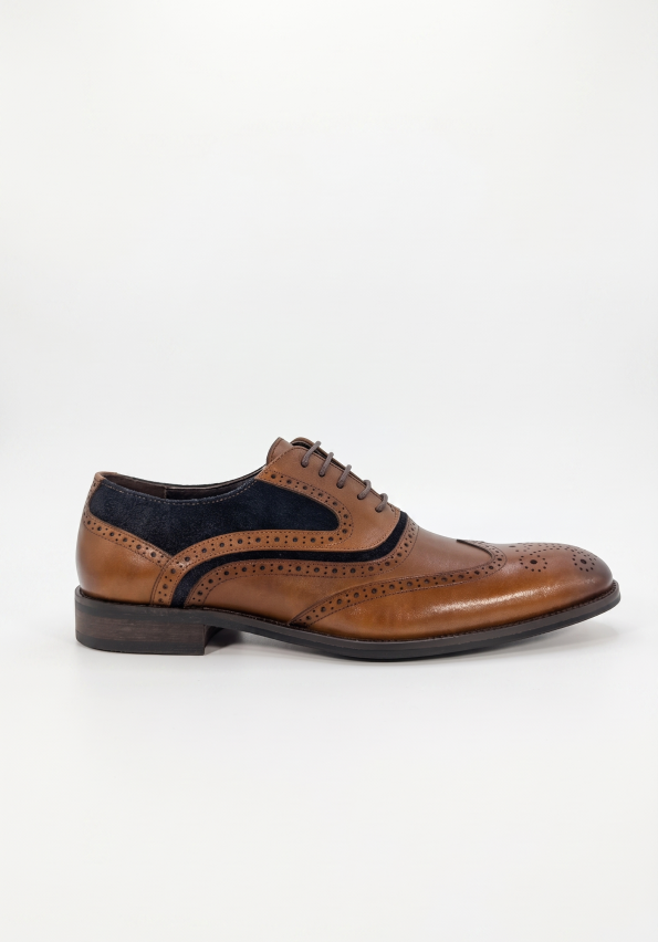 Side profile of a premium tan leather men's wingtip brogue shoe with navy suede side panels, decorative perforations, and a stacked heel against a clean white background.