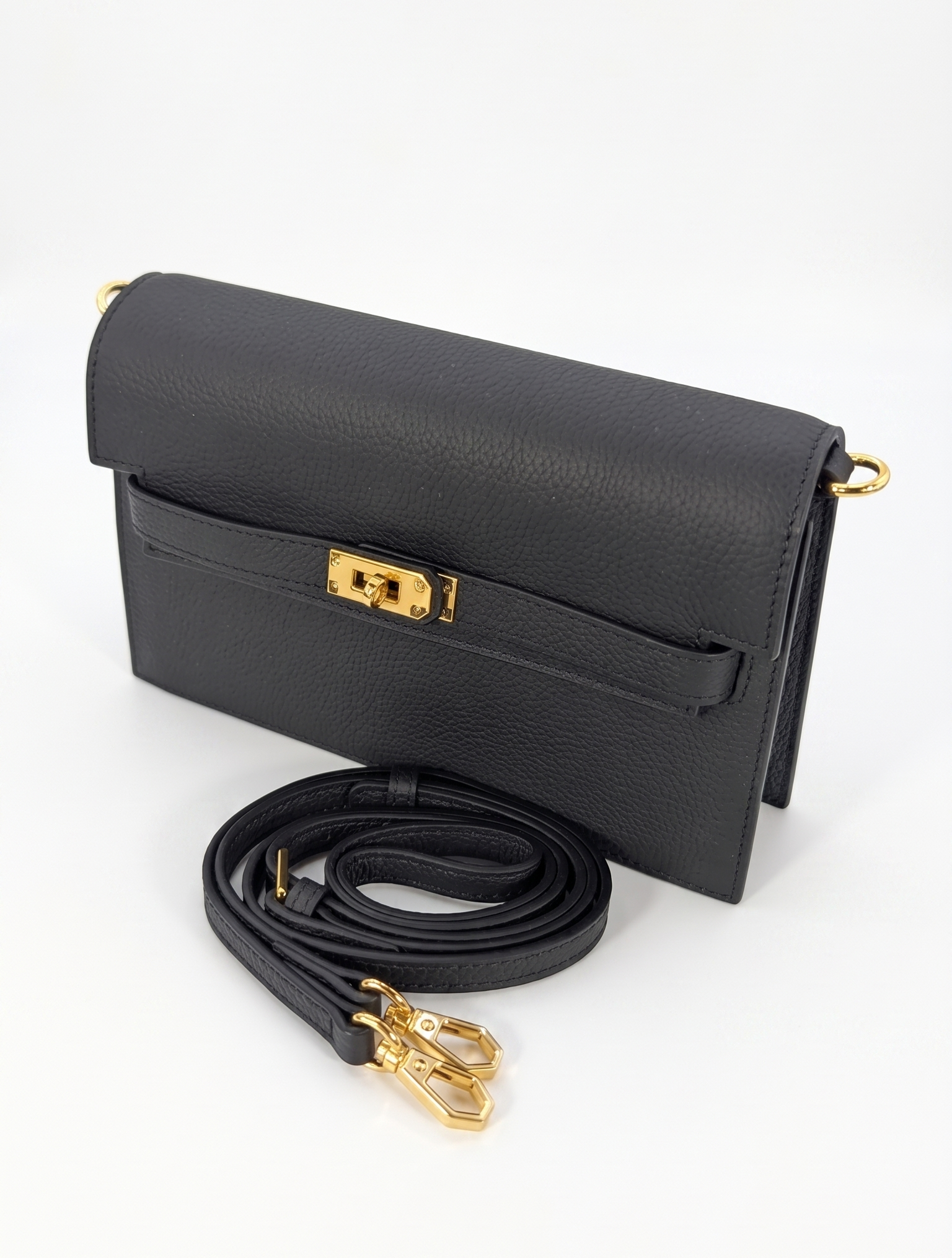 SHUCLUB Luxury Pebbled Leather Wallet-on-Chain Clutch – Noir Black Front View: Noir black pebbled leather wallet-on-chain clutch by SHUCLUB, featuring a structured rectangular profile, a horizontal front strap accented with a gleaming gold-tone turn-lock clasp, and a matching detachable leather shoulder strap on a solid white background. Back View: Rear view of the black pebbled leather SHUCLUB clutch highlighting a clean, seamless exterior slip pocket, hand-painted edge glazing, and gold-tone d-rings with a coiled leather strap.