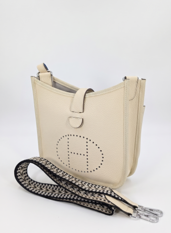 A centered shot of a cream-colored pebbled leather crossbody messenger bag featuring a thick, comfortable shoulder strap with a vibrant blue underside on a pure white background