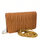 A camel tan matelassé textured leather crossbody bag by SHUCLUB, showcasing a unique vertical quilted design, an interwoven leather and gold-tone chain strap, and a decorative gold charm featuring a circular mirror, shot against a solid white studio background.